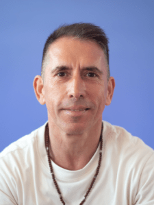 The image showcases a middle-aged Hispanic man, his face sporting a slight smile as he looks directly into the camera.