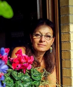 The image portrays a middle-aged woman with dark hair and glasses, gazing out her front door, with purple and red flowers in the foreground.